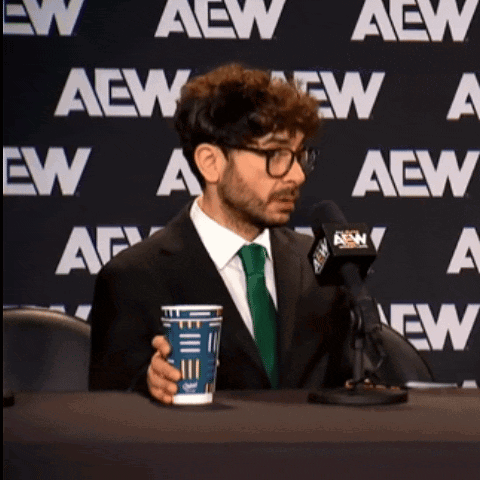 Tony Khan sits at an AEW press conference holding a drink and looking worried.