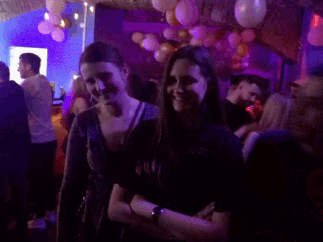two women are posing for a picture in a dark room with balloons hanging from the ceiling