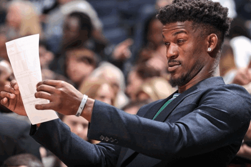 Jimmy Butler holds a sheet of paper and studies it with confusion.