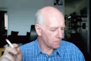 An older man looks down pensively while holding a cigarette.