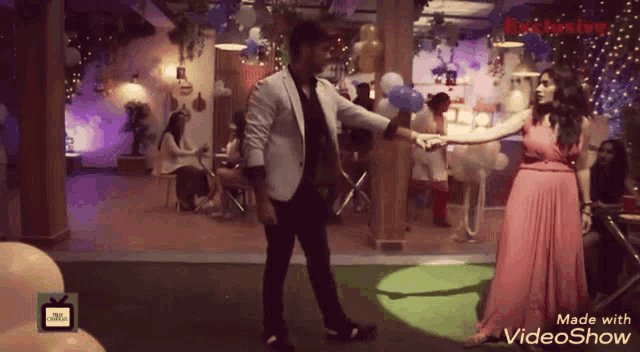 a man in a white jacket is dancing with a woman in a pink dress in a video show