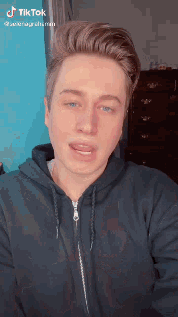 a young man wearing a blue hoodie has a tiktok sticker on his face