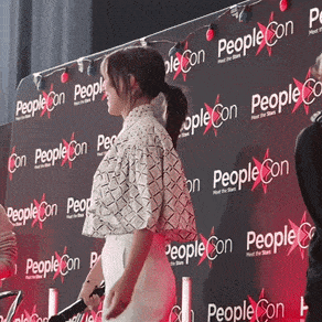 a woman stands in front of a wall with people con written on it