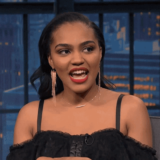 a woman wearing earrings and a necklace looks at the camera with her mouth open