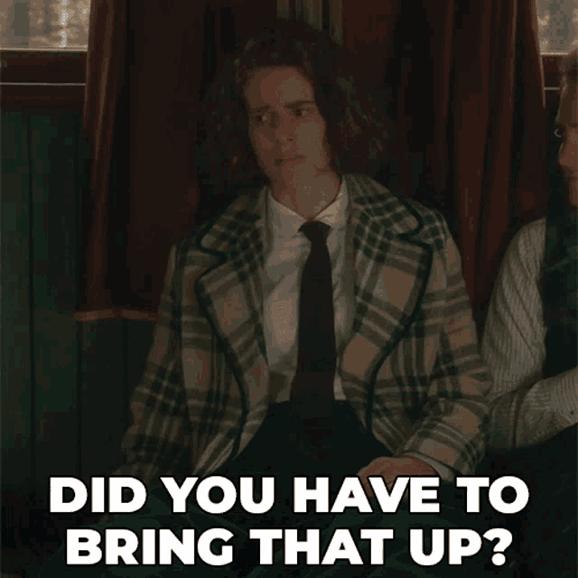 a woman wearing a plaid jacket and tie is sitting next to a man who says did you have to bring that up