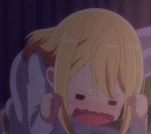 A blonde anime girl rests her head in her hands, looking upset.