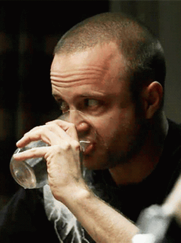 A man drinks water while looking uncomfortable in a Breaking Bad scene.