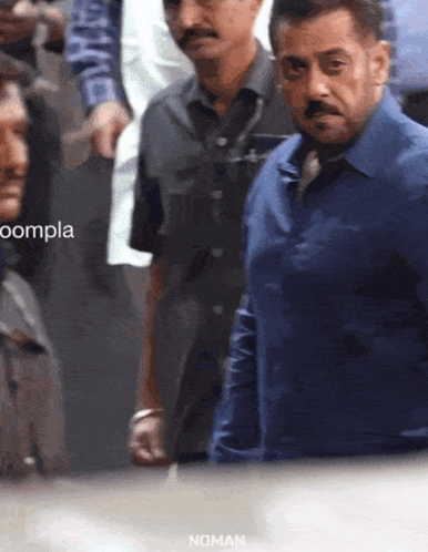 a man in a blue shirt stands in a crowd with the word noman on the bottom