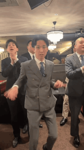 Several men in suits perform a synchronized dance indoors.