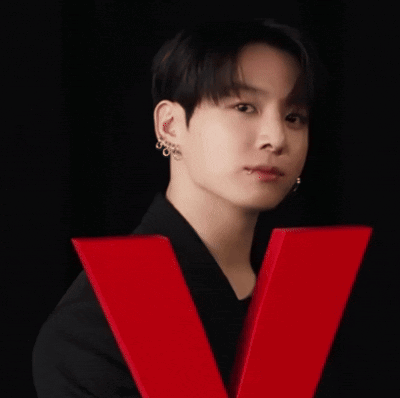 A man in black poses against a black backdrop with a large red V shape.