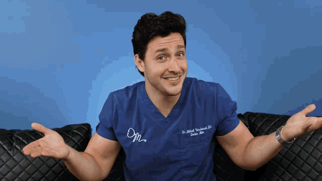 A man in blue scrubs raises both hands in an explanatory shrug.