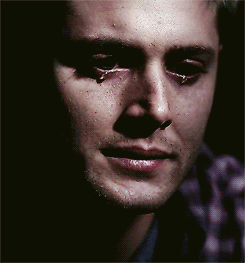 Dean Winchester looks tearful in a dark close-up.