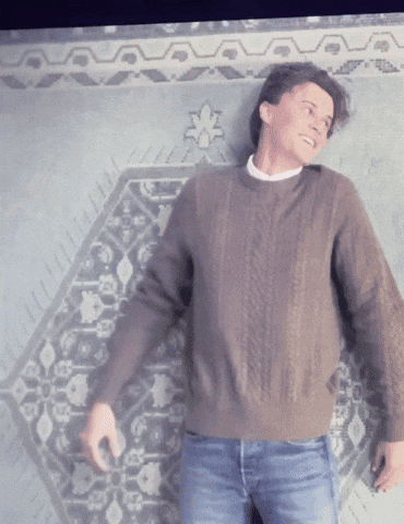 a man in a brown sweater is standing in front of a wall with a pattern
