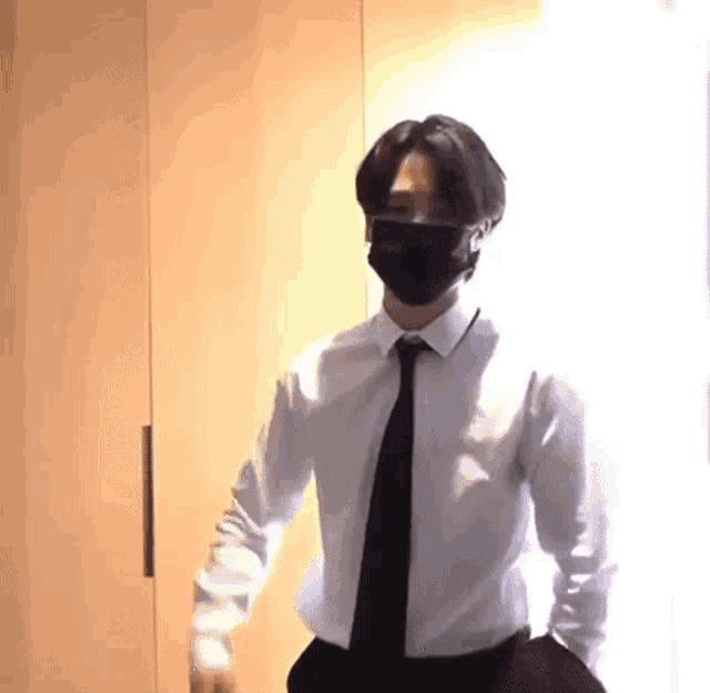 a man wearing a white shirt and black tie is wearing a mask .
