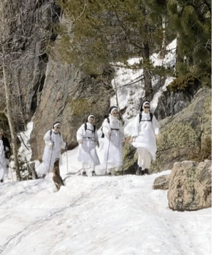 a group of people walking in the snow wearing white clothes