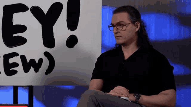 RJ City sits before the “HEY! (EW)” background, speaking toward someone offscreen.