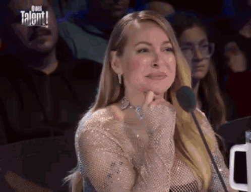 a woman is sitting in front of a microphone with her hand to her chin .