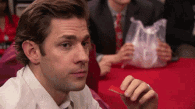 Jim Halpert from The Office gives a skeptical sideways look while seated at a table.