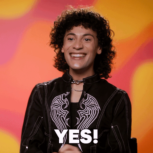 a man with curly hair is smiling and wearing a black jacket that says yes