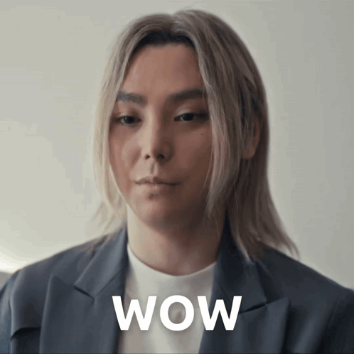 a woman with long blonde hair is wearing a grey jacket and a white shirt and has the word wow written on her face
