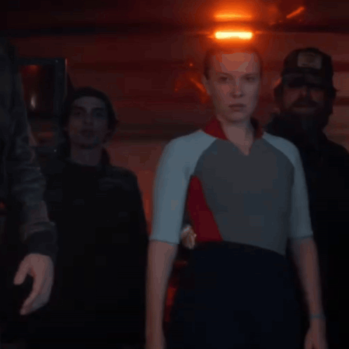 a woman in a wetsuit is standing next to two men in a dark room with a red light behind them .