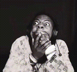 A person wearing headphones covers their mouth with a startled expression.