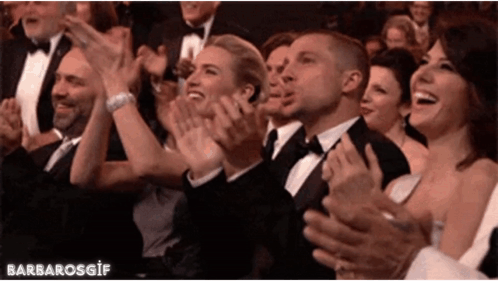 A formally dressed crowd applauds at an event.