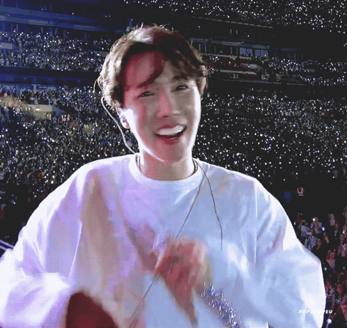 a man in a white shirt is smiling in front of a crowd of people in a stadium .