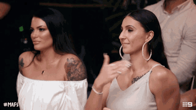 two women are sitting next to each other and one has a tattoo on her arm