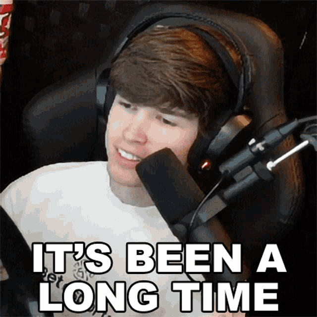 a man wearing headphones is sitting in front of a microphone with the words it 's been a long time above him