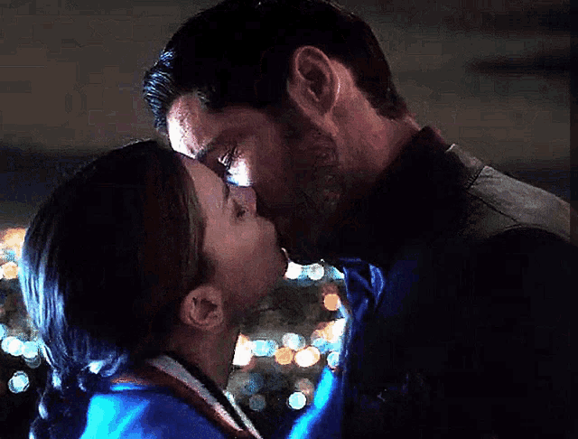 a man and woman are kissing in front of christmas lights