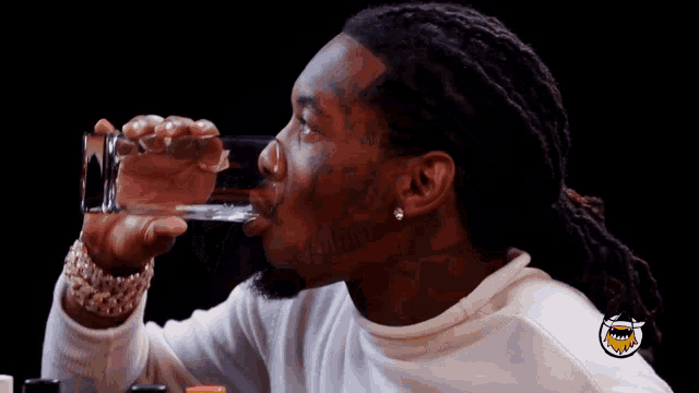 a man drinking from a glass with a tattoo on his face that says ' believe '