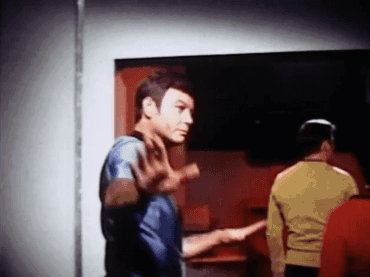 a man in a blue shirt is standing in a room with other men and making a stop sign .