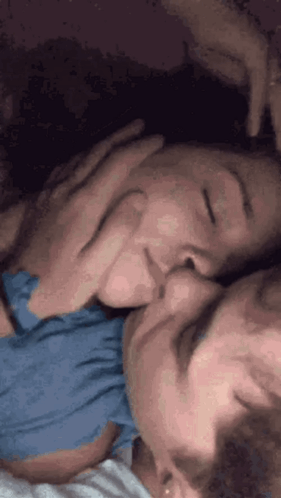 A couple cuddle closely in bed, with one resting on the other.