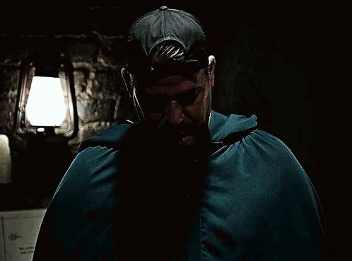 a man in a cape covering his face with his hands in a dark room