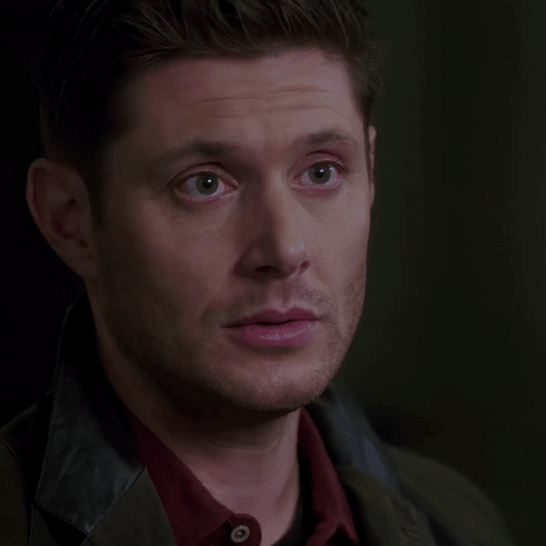 A man in a dark scene looks ahead with a faint smile.
