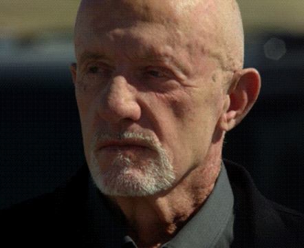 a bald man with a beard is wearing a black jacket and a grey shirt