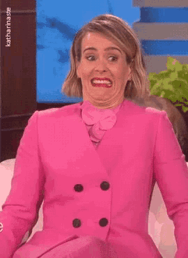 A woman in a bright pink suit makes an anxious, uncomfortable grimace.
