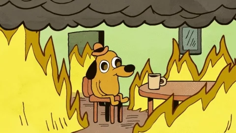 The “This Is Fine” dog calmly drinks at a table while flames surround the room.