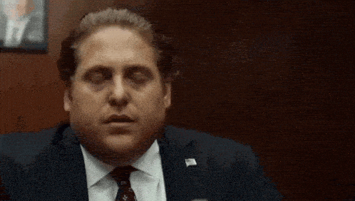 Man in a suit glances down, looking unimpressed.
