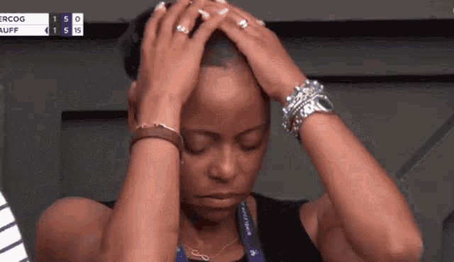 A woman sits with both hands pressed to her head in a tense reaction.