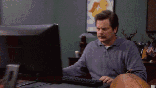 Ron Swanson throws a computer into a trash can at his desk.