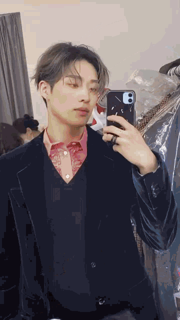 a man in a suit is taking a selfie with his phone in a dressing room .