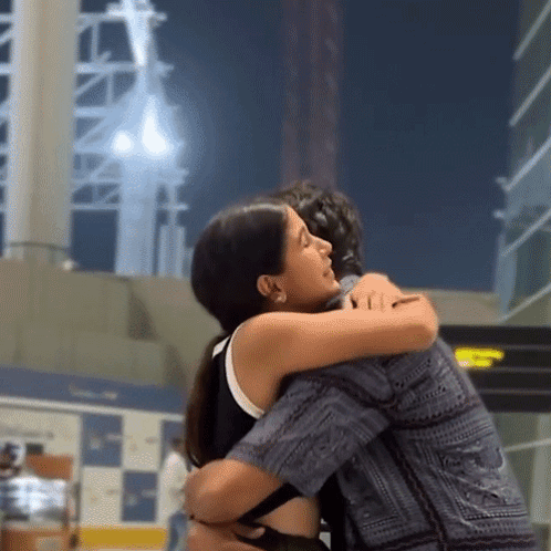 Two people embrace tightly in a bright public indoor space.