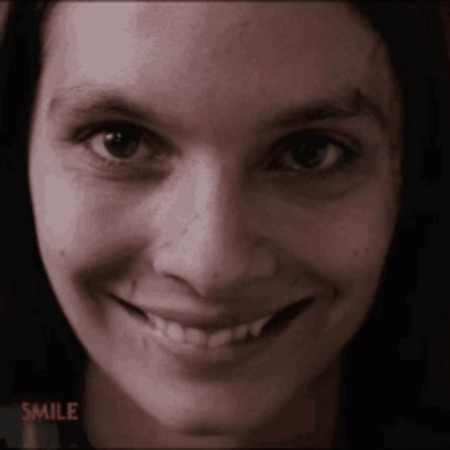 A close-up person gives an unsettling wide smile in dim light.