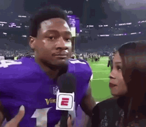 A football player in a purple jersey gives a skeptical sideways look during an interview.