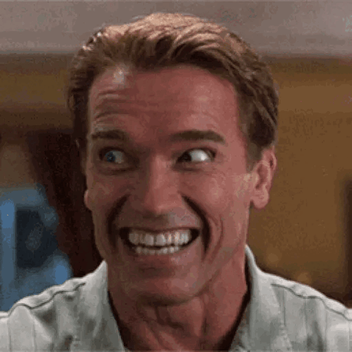 A man makes an exaggerated wide-eyed, toothy nervous grin.