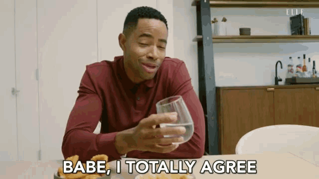a man is sitting at a table holding a glass of water and says babe i totally agree