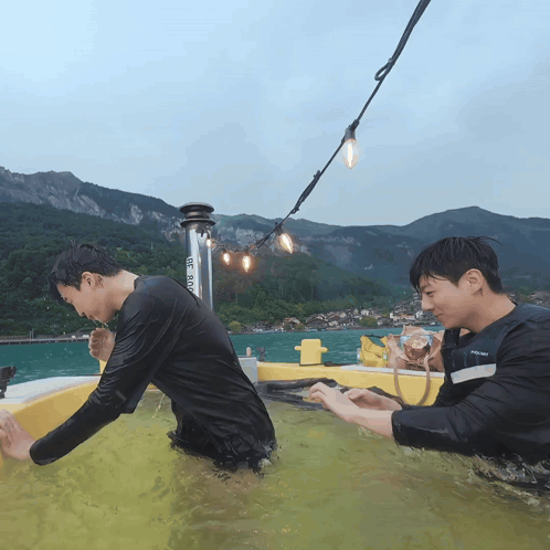 Two men playfully interact outdoors at a grassy campsite under string lights.