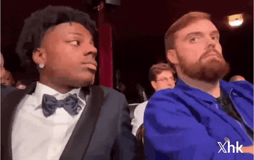 Two men seated at an event exchange an uncomfortable sideways look.